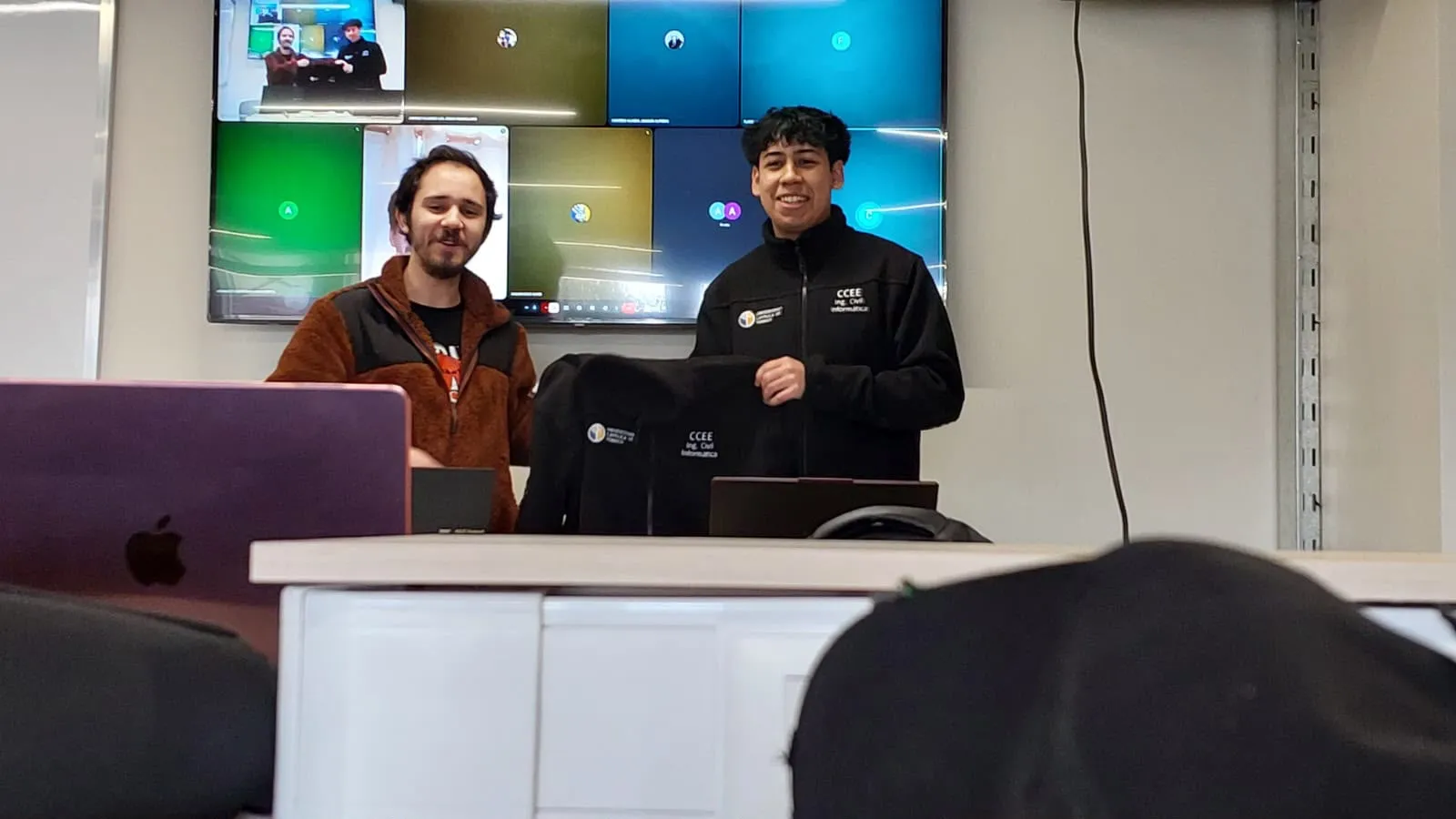 Dos integrantes del CCEE sonríen frente a la pantalla de la sala durante el cambio de mando